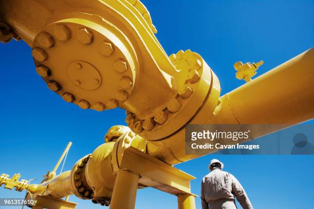 male worker standing below yellow painted pipeline at oil refinery - oil industry stock-fotos und bilder