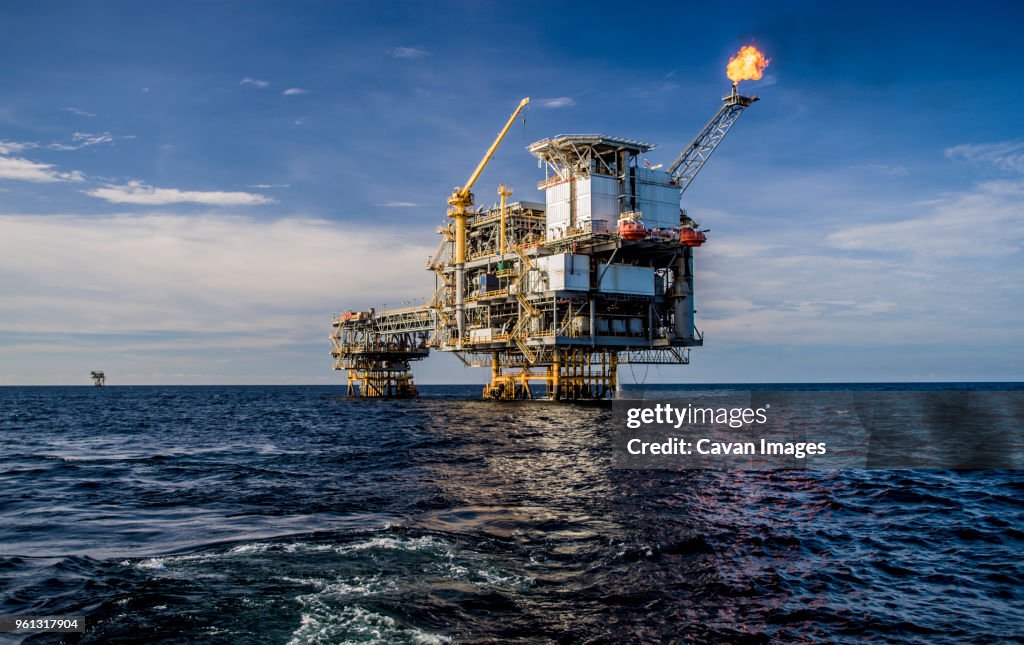 Offshore platform in sea against cloudy sky