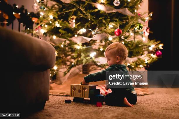 side view of cute baby boy playing with toy truck by christmas tree at home - christmas toys stock pictures, royalty-free photos & images