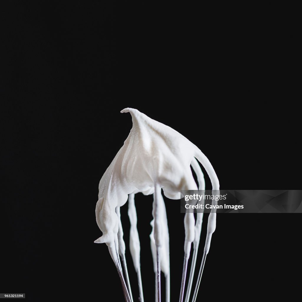Close-up of whipped cream on wire whisk against black background