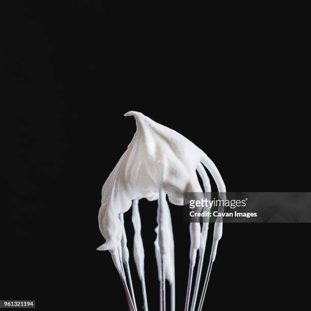 close-up of whipped cream on wire whisk against black background - natas batidas imagens e fotografias de stock