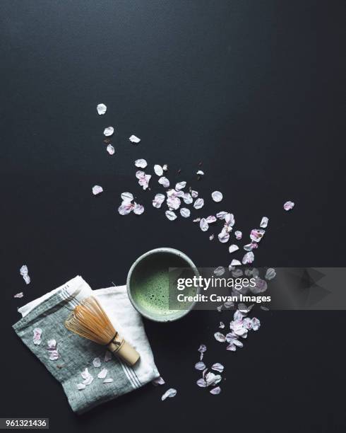 overhead view of matcha tea and bamboo whisk by petals on black background - black bamboo stock pictures, royalty-free photos & images