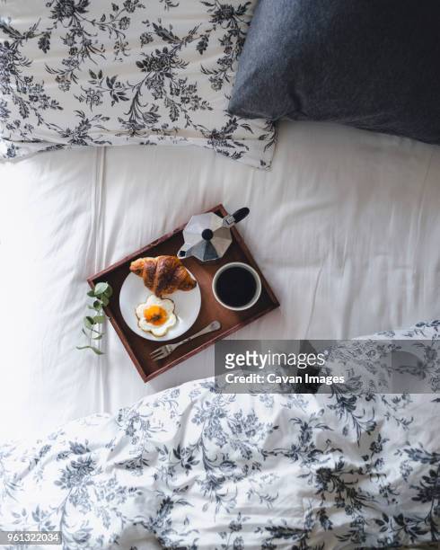 overhead shot of breakfast tray loaded with croissant, fried egg and coffee on bed - breakfast in bed tray stock-fotos und bilder