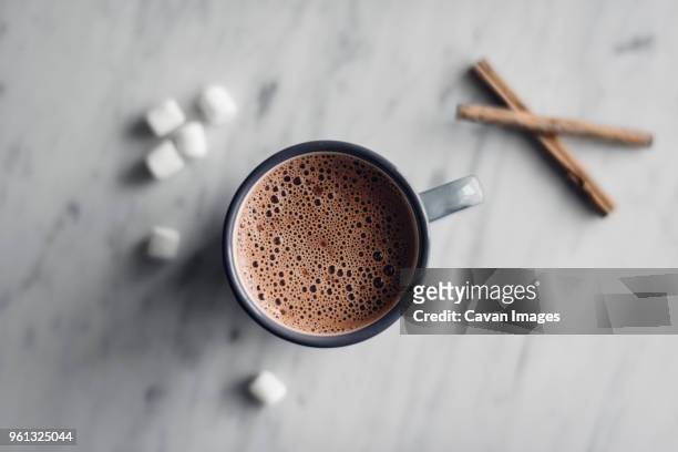 overhead view of frothy hot chocolate in mug with marshmallows and cinnamon on table - hot chocolate stock pictures, royalty-free photos & images