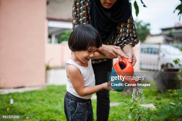 midsection of woman with son watering plants in backyard - islamic action front stock pictures, royalty-free photos & images