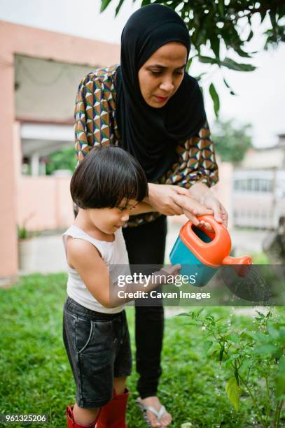 mother with son watering plants in backyard - islamic action front stock pictures, royalty-free photos & images