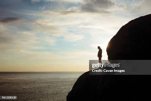 silhouette man standing on rocky mountain by sea against sky - anchorage foto e immagini stock