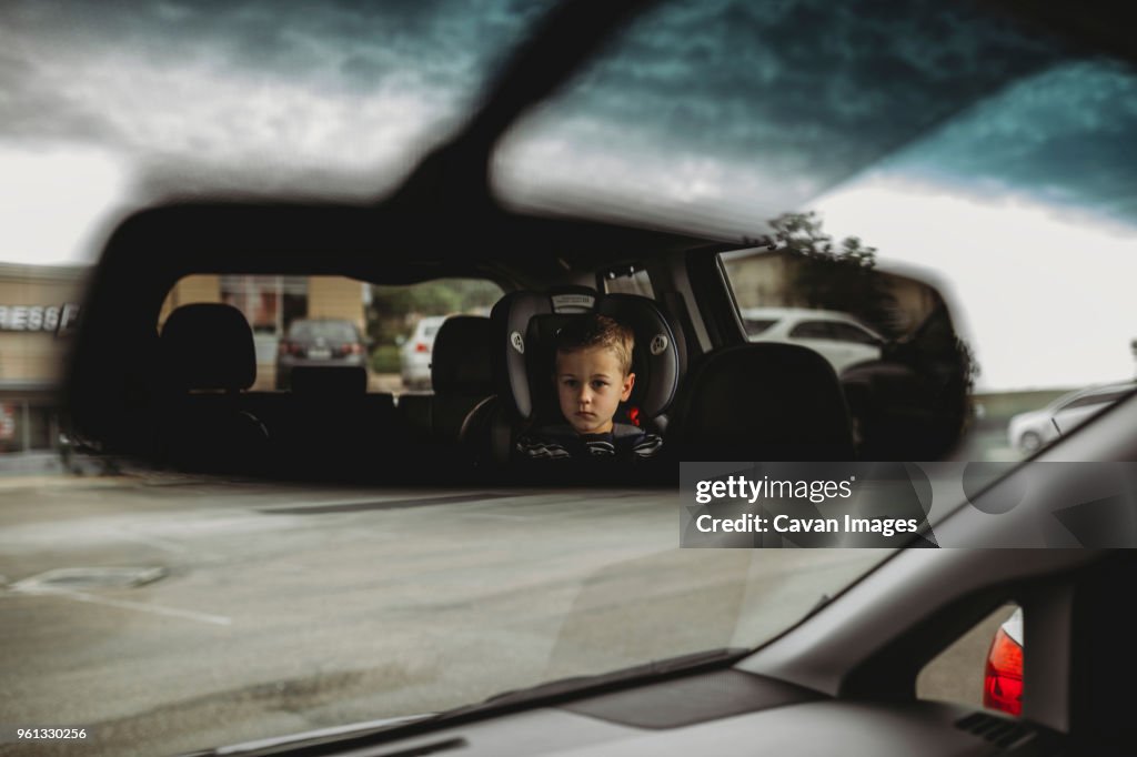 Reflection of boy on rear-view mirror in car