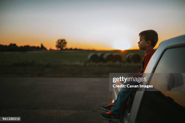 side view of boy looking away while sitting on pick-up truck during sunset - truck side view stock pictures, royalty-free photos & images