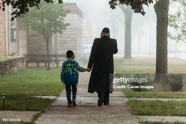 rear view of father and boy walking on footpath during foggy weather - judaism stock-fotos und bilder