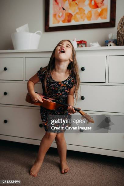 full length of girl playing guitar while standing at home - child singing stock-fotos und bilder