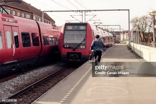 rear view of businessman running on railroad station platform - arrivo corsa foto e immagini stock