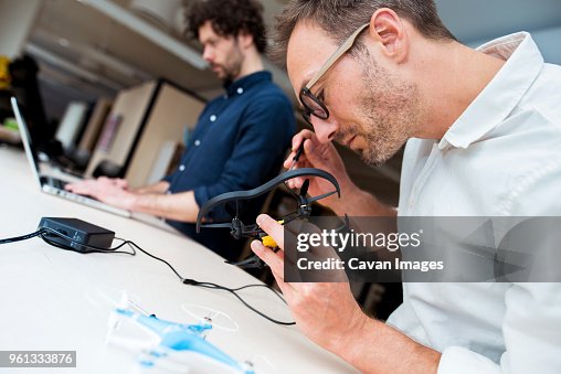 Engineer examining drone while coworker using laptop computer in office Engineer examining drone while coworker using laptop computer in office