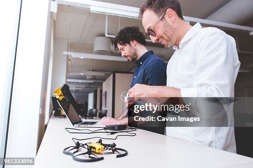 Technician examining drone while coworker using laptop computer in office Technician examining drone while coworker using laptop computer in office