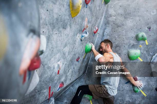 determined athlete climbing on rock wall at gym - bouldering - fotografias e filmes do acervo