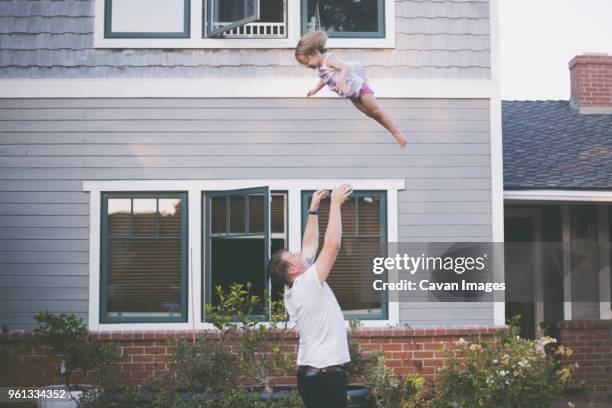 playful father throwing daughter in air while standing in backyard - dad throwing kid in air imagens e fotografias de stock