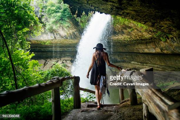 rear view of woman walking towards waterfall in forest - behind waterfall stock-fotos und bilder