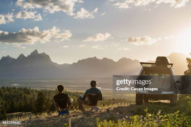 rear view of male hikers relaxing on reclining chair in field - sitting on a cloud foto e immagini stock