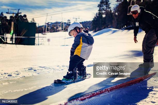 father assisting daughter in snowboarding on sunny day - genderblend2015 stock pictures, royalty-free photos & images