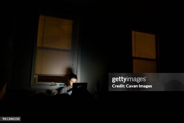 woman using laptop computer in darkroom at home - dark room stock-fotos und bilder