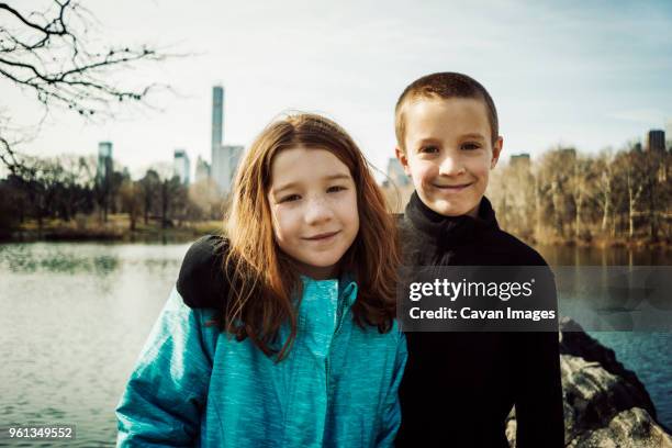 portrait of smiling brother with arm around sister at lake in park - skinhead girls - fotografias e filmes do acervo