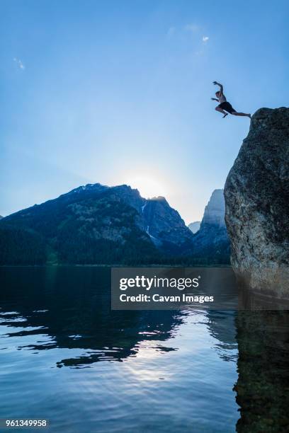 low angle view of teenage boy cliff jumping into river against sky - salto desde acantilado fotografías e imágenes de stock