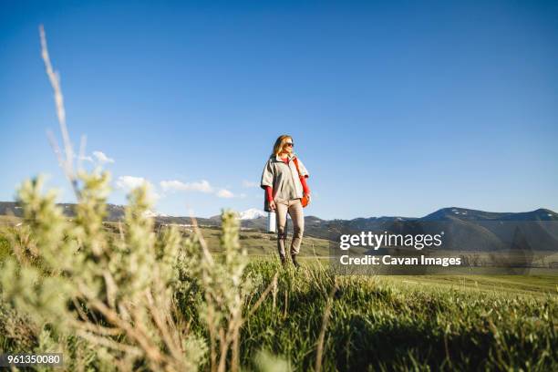 female hiker walking on field against sky - mid adult women stock pictures, royalty-free photos & images