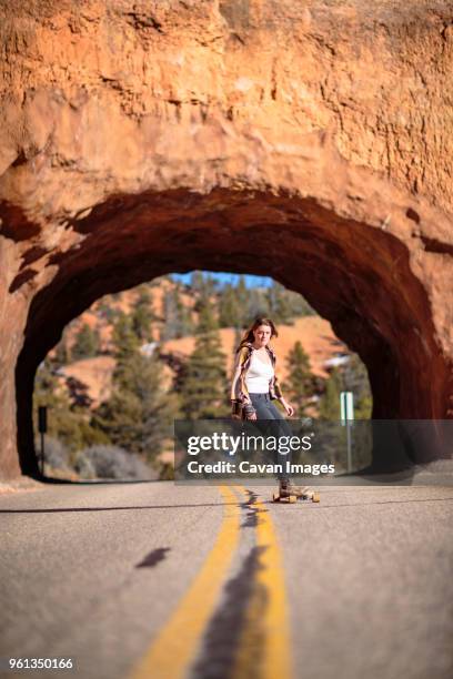 hiker skateboarding on road against rocky tunnel at bryce canyon national park - rocky road stock pictures, royalty-free photos & images