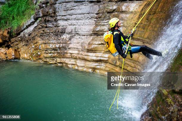 side view of woman rappelling down into lake - canyoneering stock pictures, royalty-free photos & images