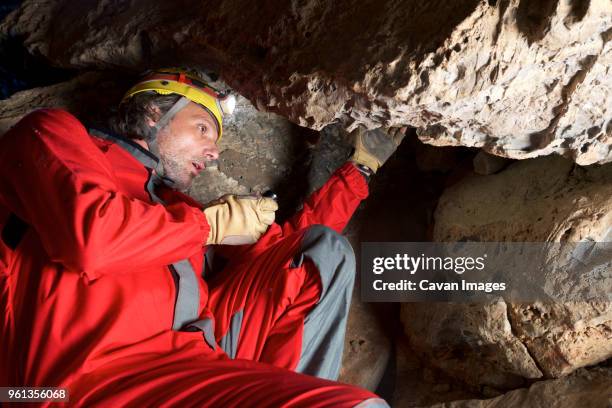 low angle view of archaeologist working on rocks while sitting in cave - archeoloog stockfoto's en -beelden