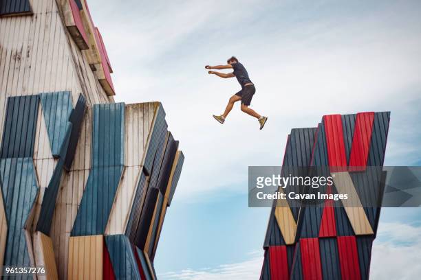 low angle view of man jumping over buildings against sky - le parkour fotografías e imágenes de stock