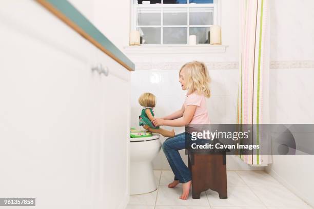 side view of girl playing with doll in bathroom at home - doll house stockfoto's en -beelden