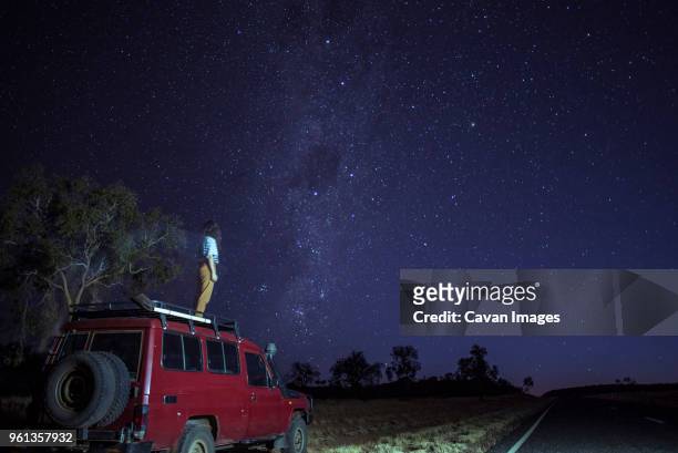 woman looking at star field while standing on car roof at desert - territorio del nord foto e immagini stock
