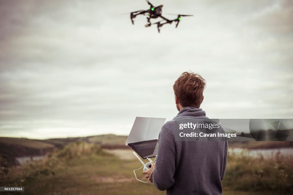 Rear view of man operating drone camera while standing on field