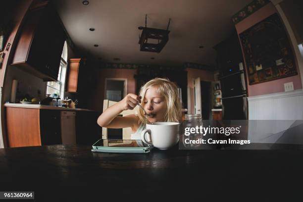 girl having food while looking at tablet computer on table - gran angular fotografías e imágenes de stock