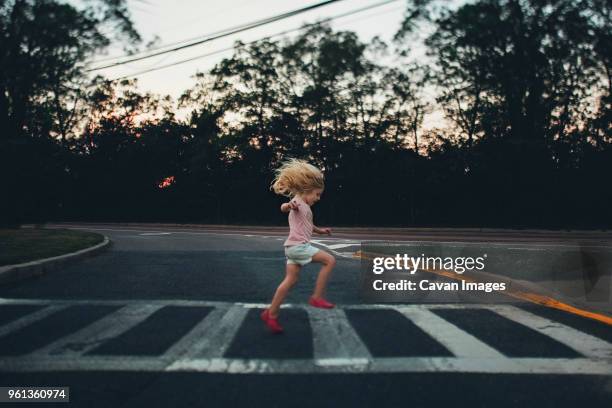 side view of girl jumping on zebra crossing against trees - zebrastreifen stock-fotos und bilder