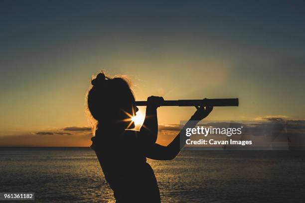 silhouette girl using telescope against sea during sunset - looking through telescope stock pictures, royalty-free photos & images