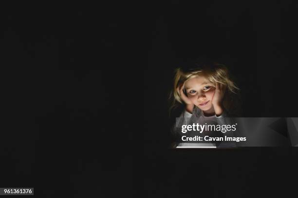 bored girl using digital tablet while sitting in darkroom at home - donkere kamer stockfoto's en -beelden