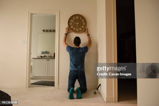 rear view of man fixing clock on wall at home - back shot position stock pictures, royalty-free photos & images