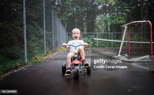 portrait of playful boy riding tricycle at playground - tricycle stock pictures, royalty-free photos & images