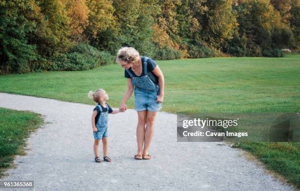 full length of mother and daughter wearing bib overalls while holding hands on dirt road - bib overalls stockfoto's en -beelden