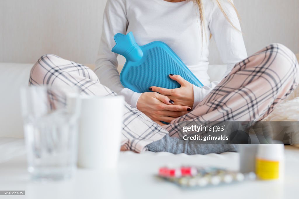 Woman with hot water bottle healing stomach pain