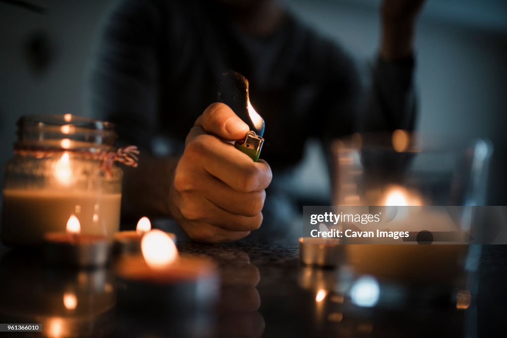 Midsection of man igniting candles with cigarette lighter on table in darkroom