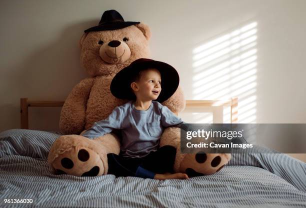 boy with teddy bear sitting on bed at home - teddy bear stock pictures, royalty-free photos & images