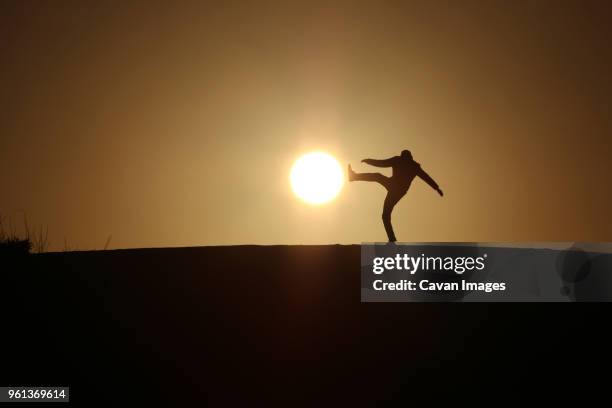 optical illusion of silhouette man kicking sun during sunset - perspective artificielle photos et images de collection