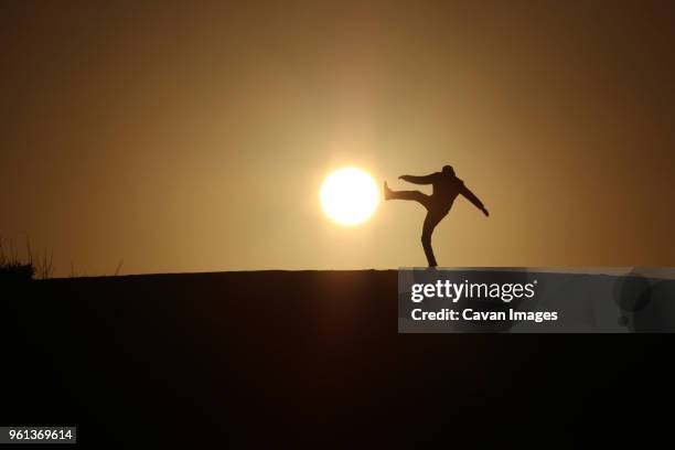 optical illusion of silhouette man kicking sun during sunset - optical illusion stock pictures, royalty-free photos & images