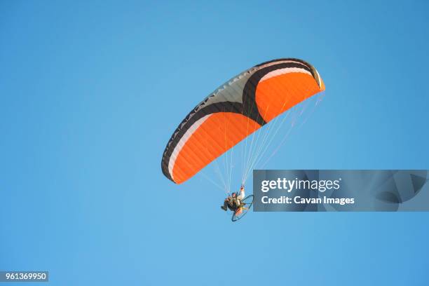 low angle view of young man motor paragliding against clear sky - motor paraglider stock pictures, royalty-free photos & images