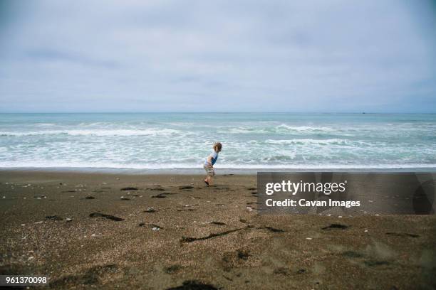 girl running on sand at beach against cloudy sky - young cheyenne stock pictures, royalty-free photos & images