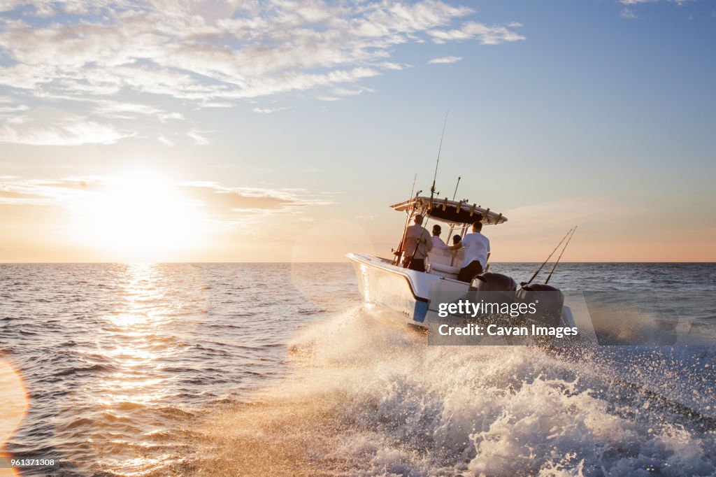 Men enjoying in speedboat at sea against sky during sunset