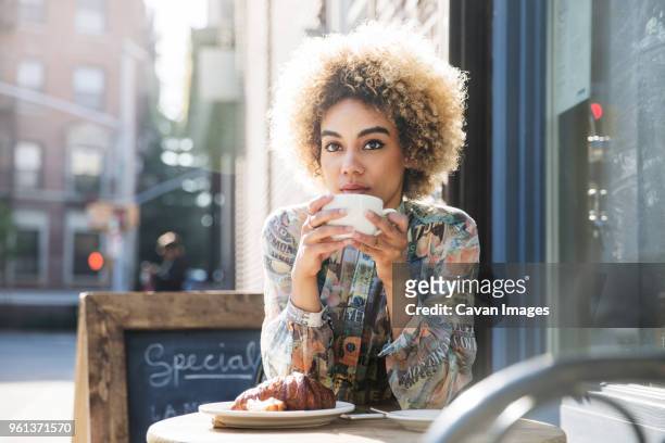 thoughtful woman holding coffee cup while sitting at sidewalk cafe - sidewalk cafe stock pictures, royalty-free photos & images